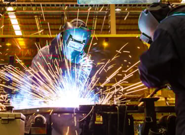 Två svetsare som svetsar i ett objekt med sprutande gnistor.