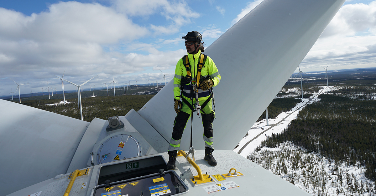 Besiktningsingenjör står längst upp på ett vindkraftverk. 