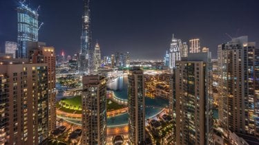 A stunning night view of a city skyline featuring tall buildings, illuminated streets, and a winding waterway.
