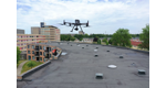 Drone hovering over a flat rooftop with surrounding buildings and trees, performing a drone inspection of the rooftop under a cloudy sky