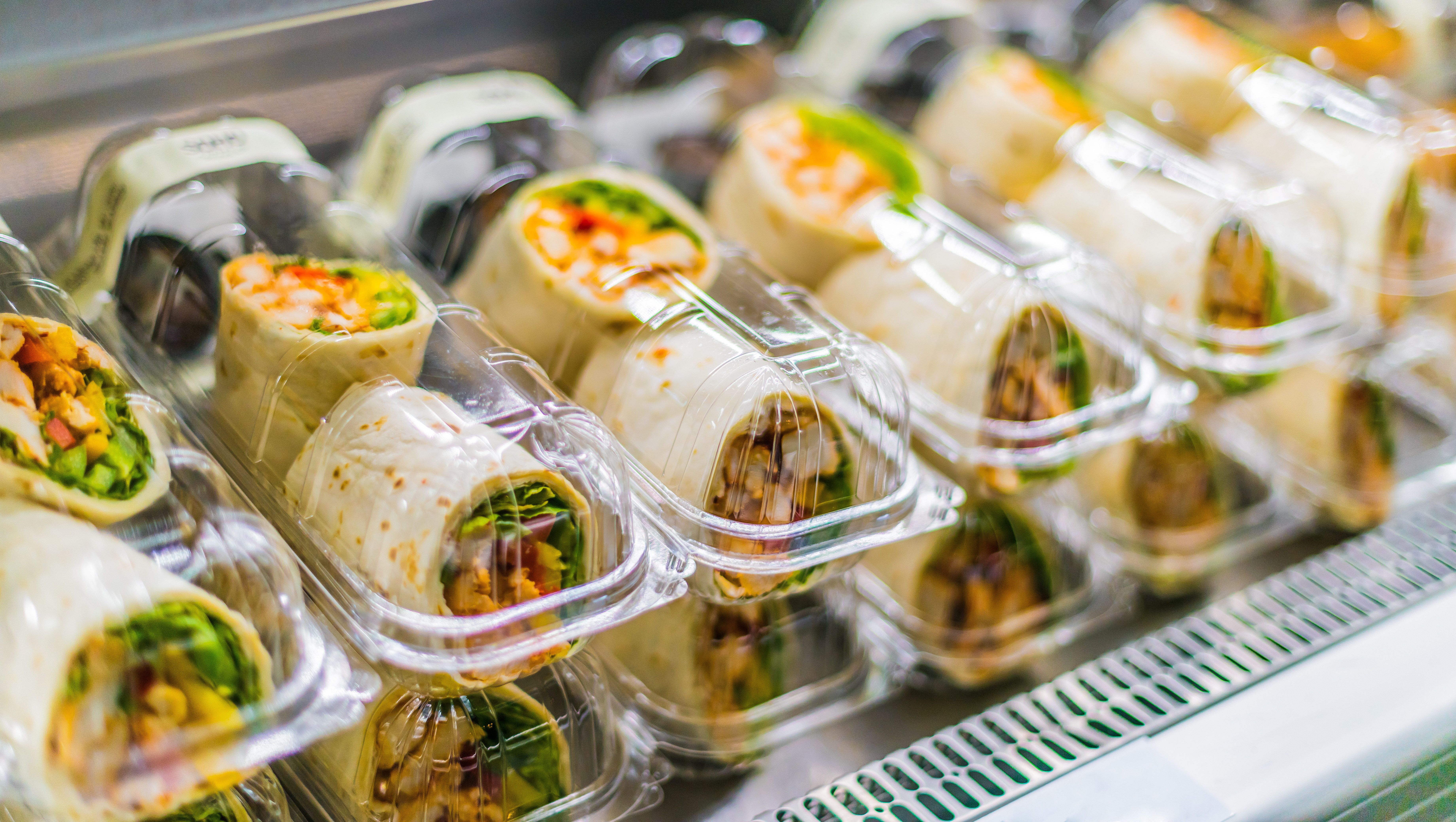 Packaged chicken wraps with fresh vegetables in clear plastic containers displayed on a refrigerator shelf