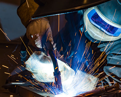 Svetsare lutar lite åt sidan medan han svetsar. Svetslågor sprutar upp.