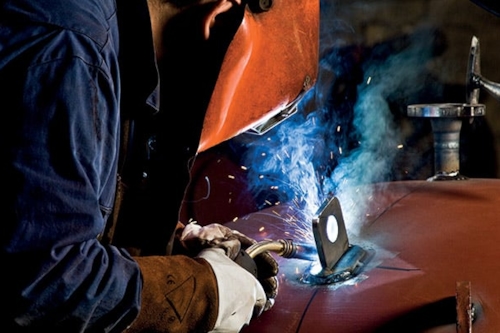 Svetsare med svetsmask lutar sig fram när han arbetar.