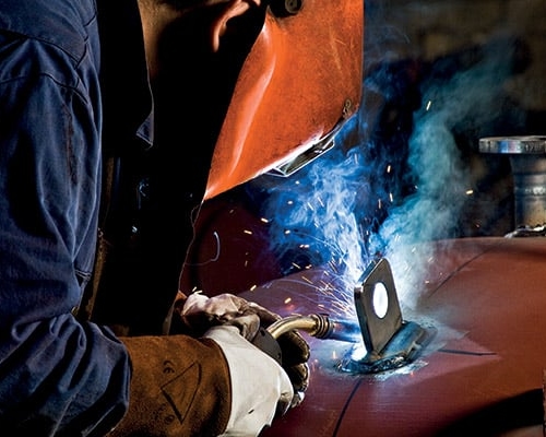 Svetsare med svetsmask lutar sig fram när han arbetar.