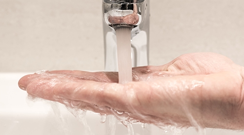 En hand över ett handfat låter vatten från en kran rinna ner i handflatan.