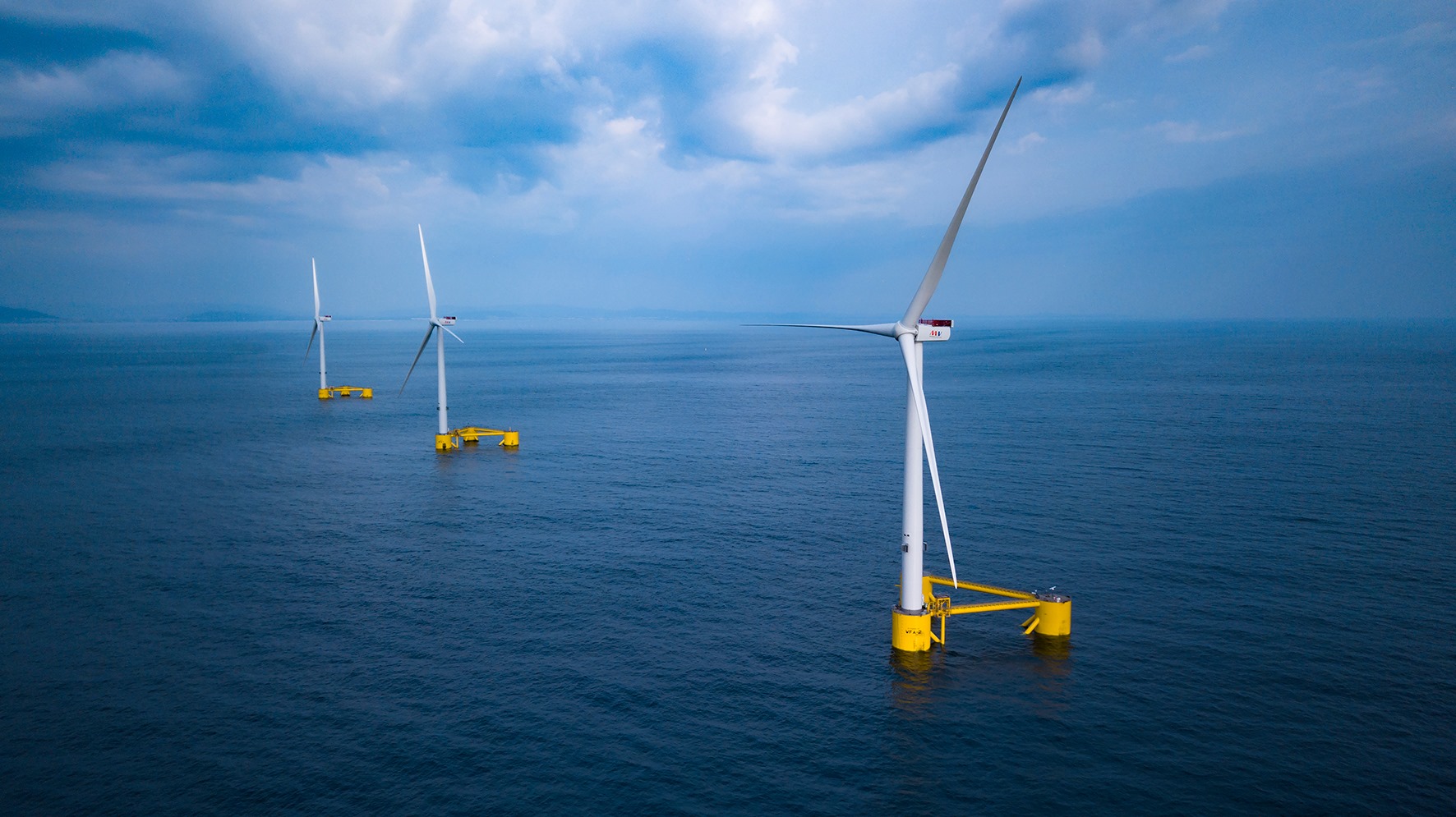 Offshore wind turbines standing in the ocean at sunset under a clear blue sky