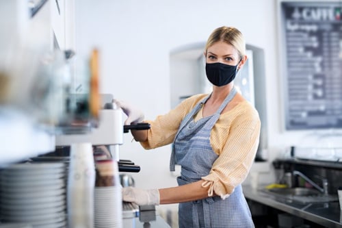 Young woman operating a coffee machine while using a quality-certified NEN-spec-1-2 face mask