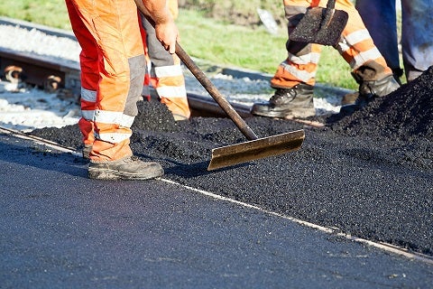 Road construction in operation with workers paving a road with asphalt