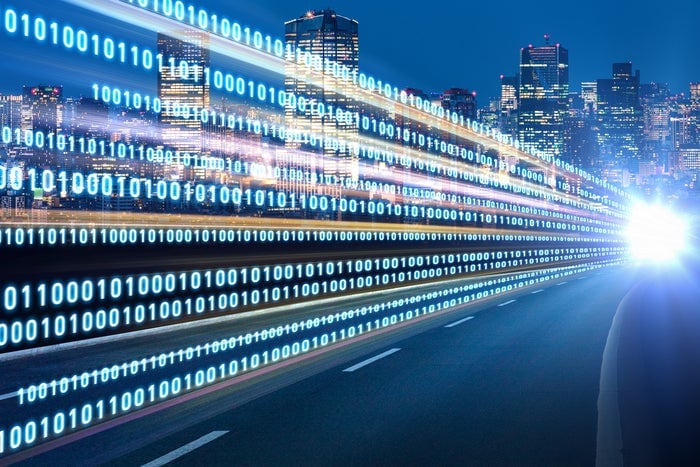 Binary code flows along a highway towards a bright city skyline at night, symbolizing digital transformation and data exchange in urban technology