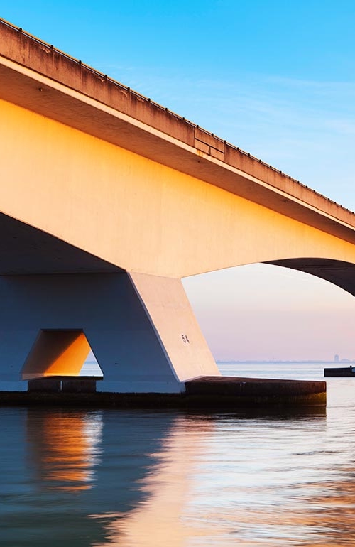 En lång modern bro av betong, över lugnt och stilla vatten.
