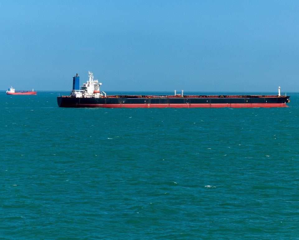 Stort lastfartyg på havet, med ett liknande fartyg längre bort, strax bakom, mot horisonten. 