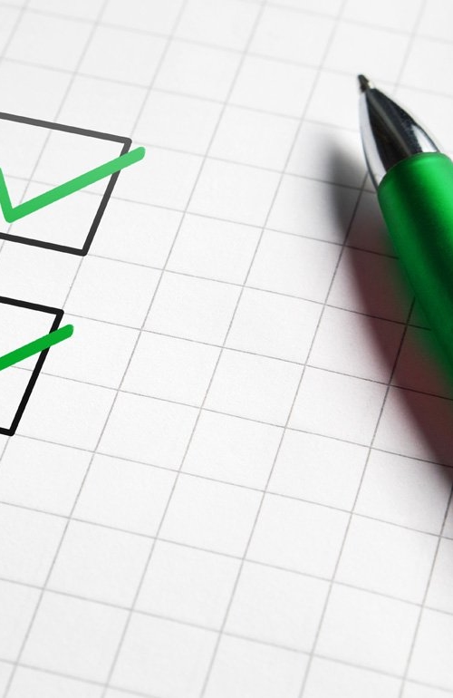 Checklista på ett rutat papper, några är avbockade med grön penna som ligger bredvid på papperet.