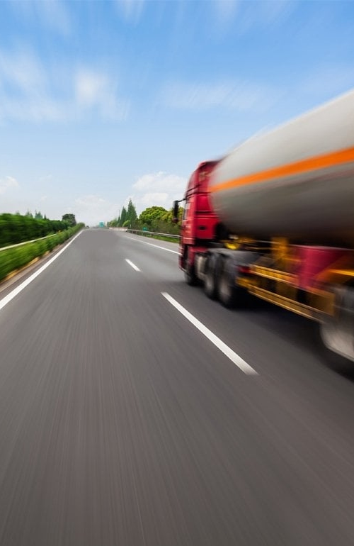En tankbil susar fram på en rak landsväg, som sträcker sig långt fram mot horisonten.