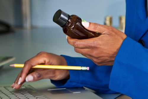 Kvinna håller i en brun flaska och en gul penna medan hon skriver på en bärbar dator.