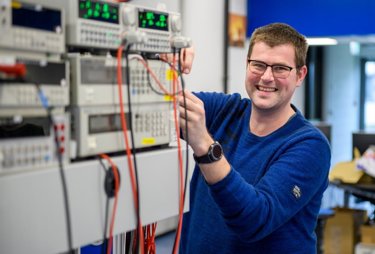 Kiwa technician Edwin Verweij, smiling in blue sweater working with electronic equipment in a laboratory setting