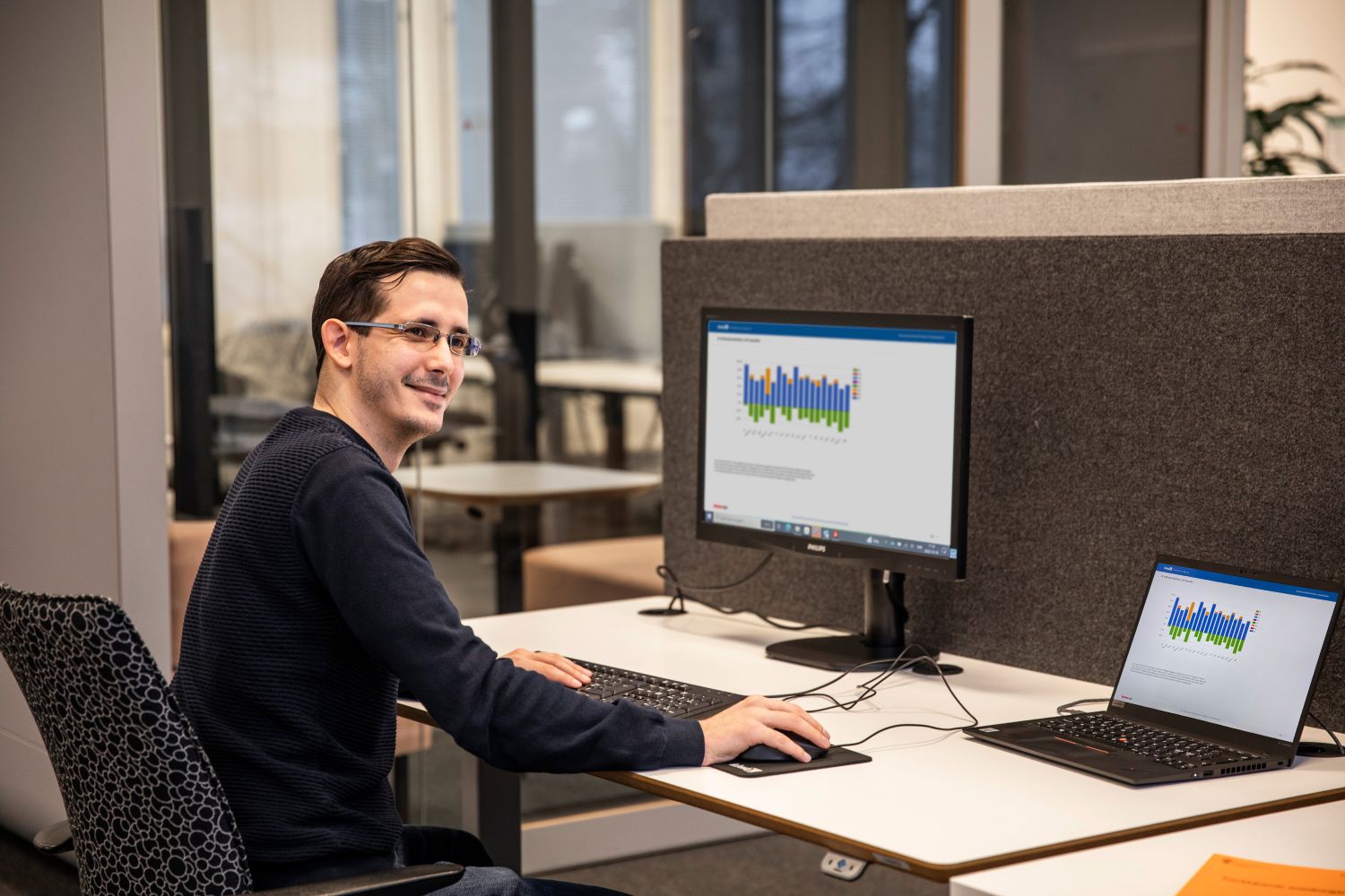 Kiwa engineer reviewing environmental data on a heat pump with lifecycle assessment charts visible on a laptop and desktop screen