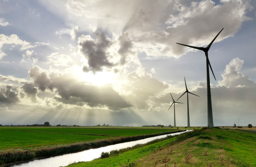 Wind turbines in a lush green landscape with a sunlit sky and dramatic clouds