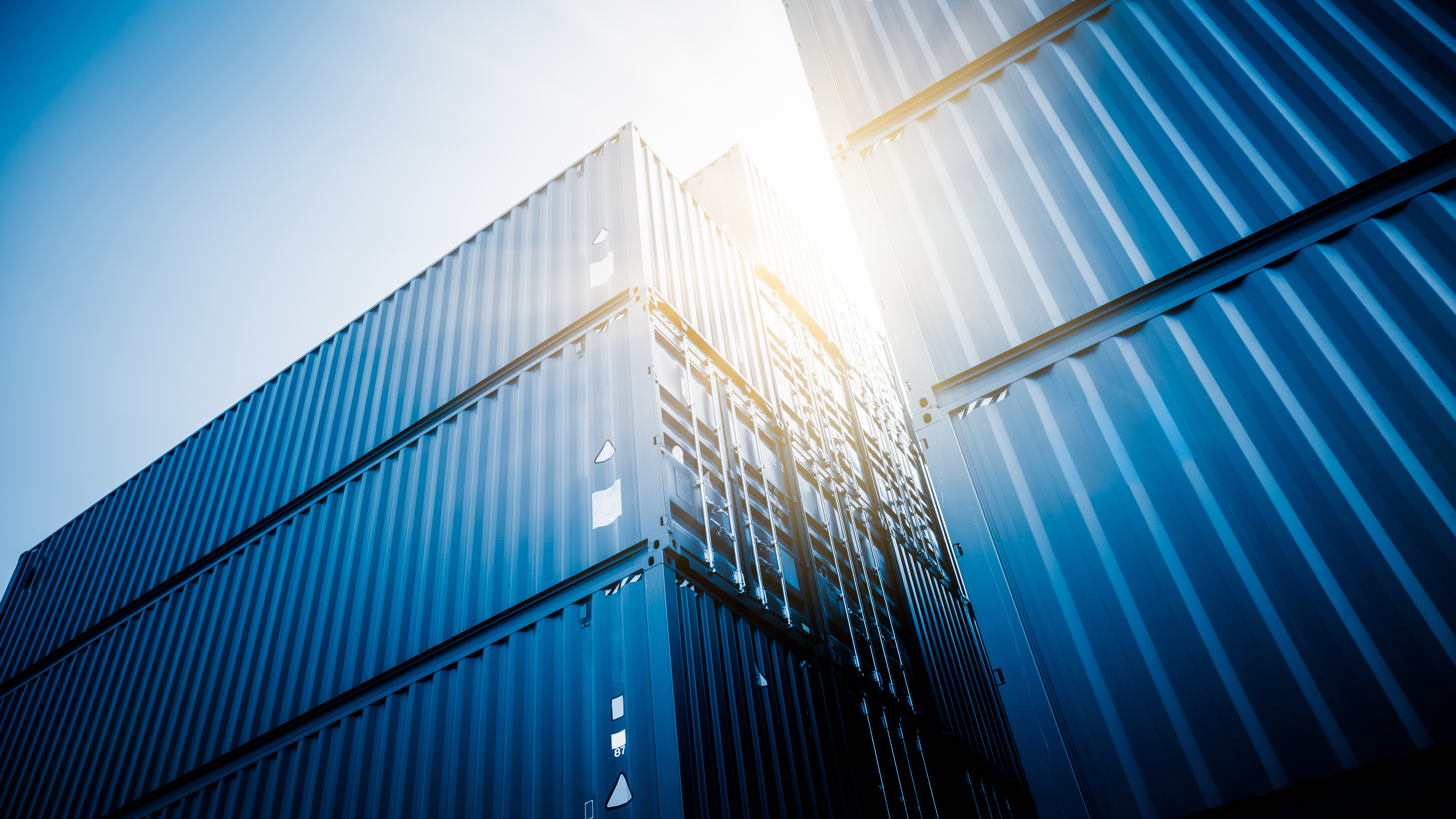 Shipping containers stacked high with sunlight shining between them, depicting industrial and transportation themes