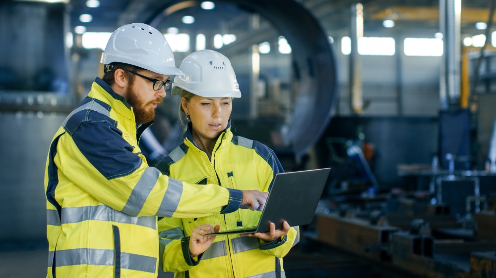 Two construction professionals reviewing CPR compliance documents with sustainability data on a laptop