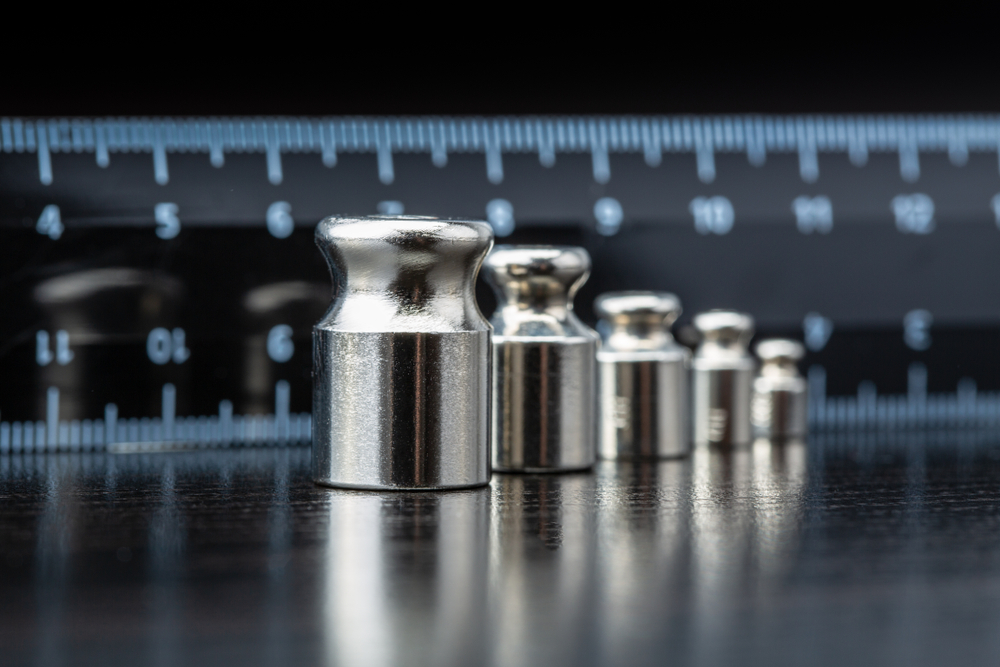 Set of metal calibration weights in ascending order with a ruler in the background on a dark surface