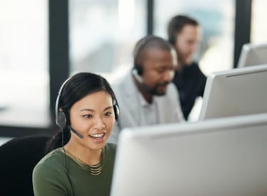 Tre personer med headset sitter i rad framför varsin datorskärm.