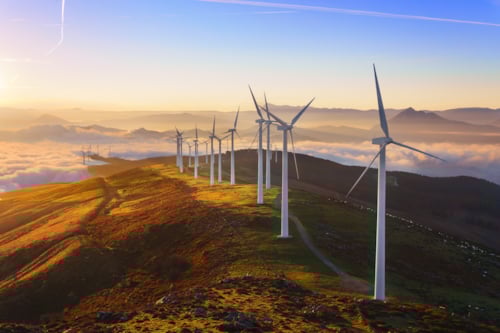 wind trubines on top of a hill during the sunset