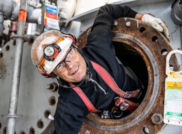 En besiktningsingenjör tittar fram från öppningen av ett slutet utrymme i ett tryckkärl.