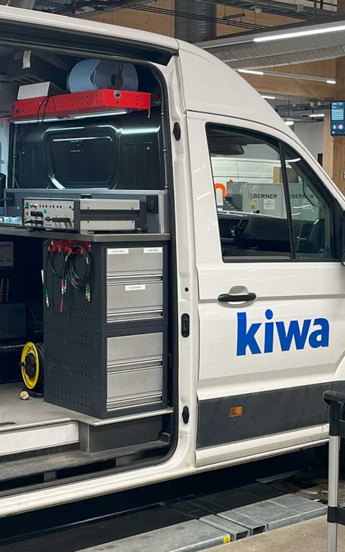 Skåpbil, endast dess vänstersida med ena framlyktan visas, som används för våra mobila kalibreringstjänster, kör på en väg.