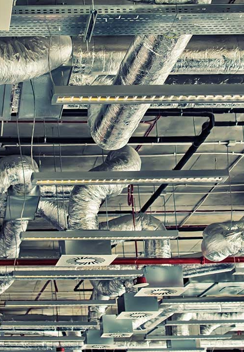 Ventilationssystem uppe i taket med flera rör och fläktar i en industrilokal.