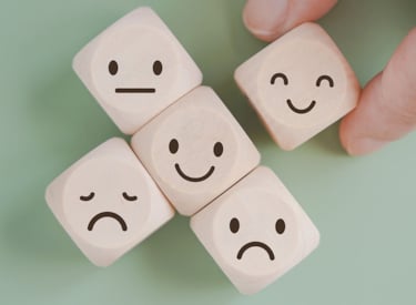 Fem tärningar som visar illustrationer av glada och ledsna ansikten i olika grader.