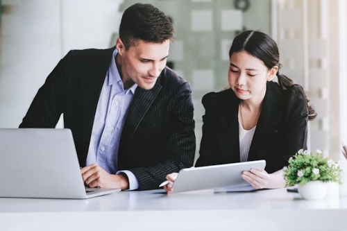 Två personer, en man och en kvinna, sitter bredvid varandra med en dator framför sig, för ISO-certifiering är dokumenterad information en viktig del i arbetet.