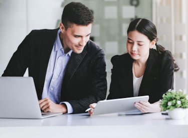 Två personer, en man och en kvinna, sitter bredvid varandra med en dator framför sig, för ISO-certifiering är dokumenterad information en viktig del i arbetet.