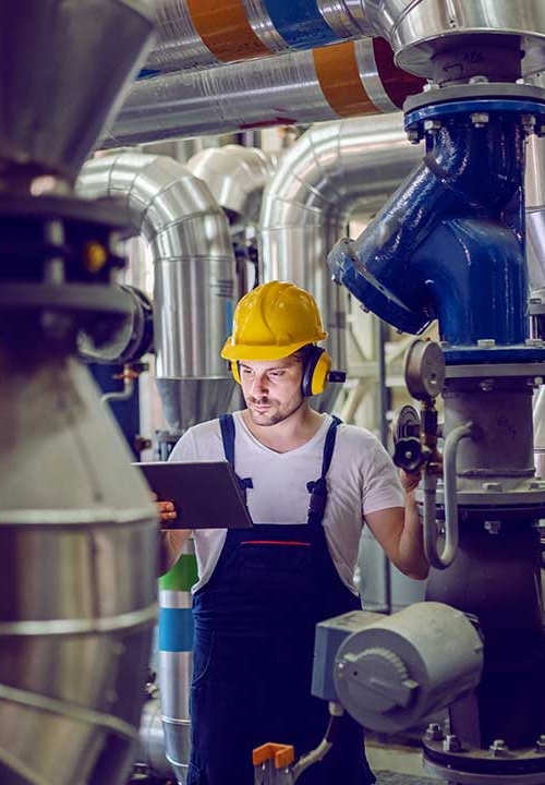 Pannoperatör med skyddshjälm justerar trycket för tryckkärl och läser instruktioner från en läsplatta.