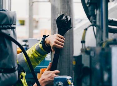 Person använder stor skiftnyckel för att justera maskin.