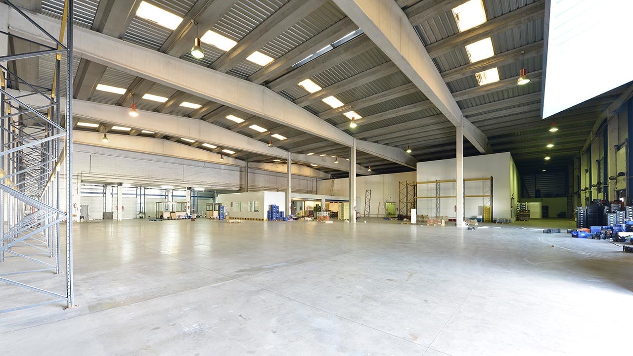 Ett stort tomt industrilager med betonggolv och takfönster i taken och betongbalkar som stödjer dem.