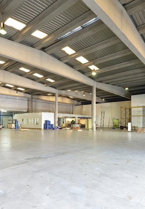 Ett stort tomt industrilager med betonggolv och takfönster i taken och betongbalkar som stödjer dem.
