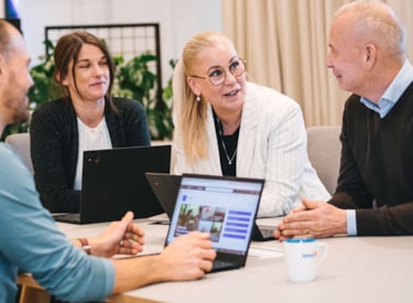 Deltagare sitter med varsin laptop och pratar runt ett bord.