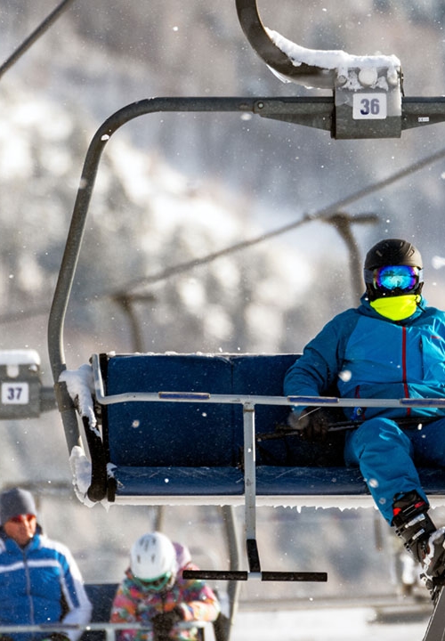 En ensam skidåkare åker en korglift uppför slalombacken, det snöar.