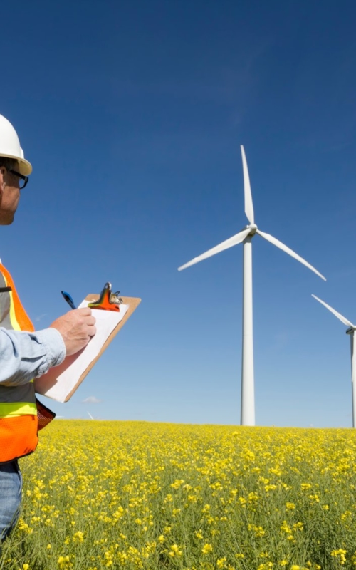 A Kiwa inspector holding a clipboard standing in front of a row of wind turbines prior to the wind turbine inspection