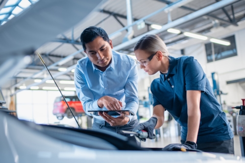 An automotive technician and an engineer collaborating on a vehicle inspection in a garage