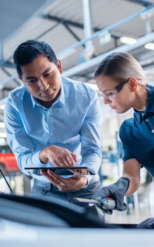An automotive technician and an engineer collaborating on a vehicle inspection in a garage