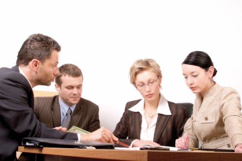 Group of four business professionals engaged in a meeting at a conference table, focused on documents