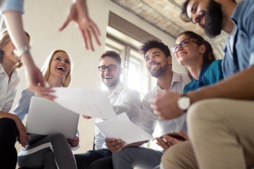 Diverse group of professionals smiling and collaborating in a modern office setting, engaging with documents and technology for teamwork success