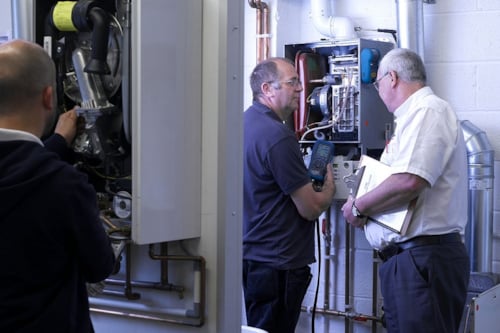 Kiwa trainer and student inspecting and repairing a gas boiler in a utility room, demonstrating boiler maintenance and troubleshooting