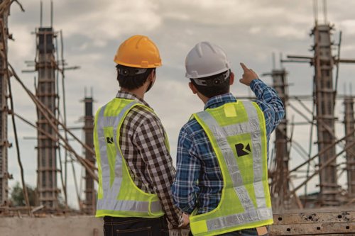 Kiwa Raba engineers in safety gear discussing building project on site with scaffolding and cloudy sky background