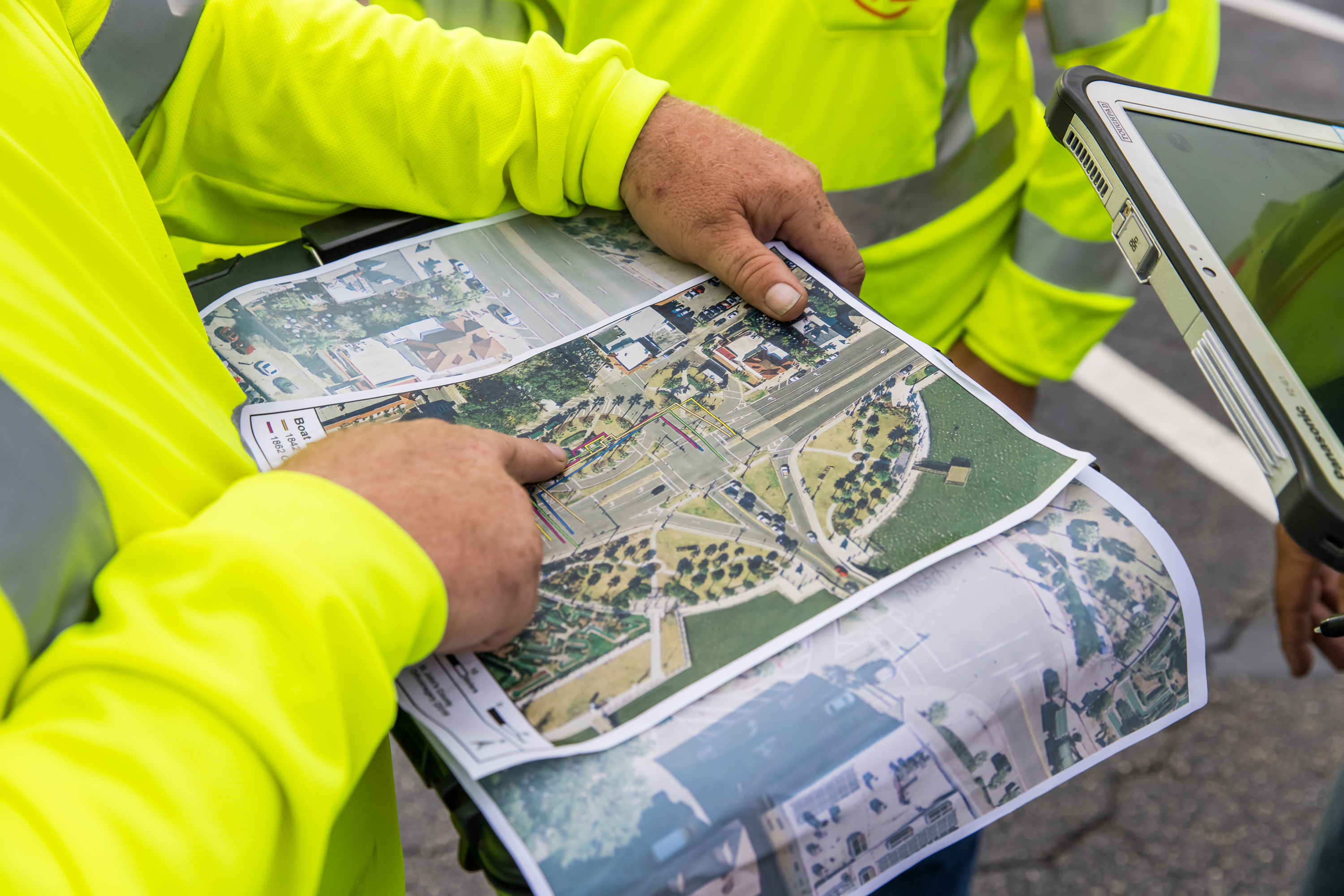 Kiwa engineers  in high-visibility safety jackets reviewing printed aerial maps and site plans on a tablet outdoors.