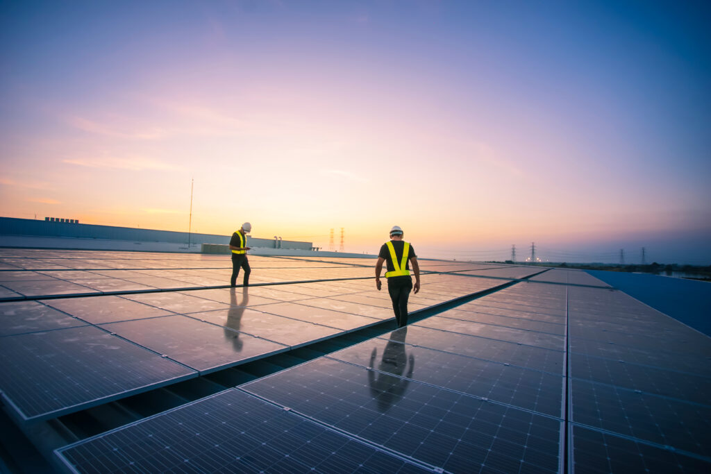 Two Kiwa inspectors in safety vests and helmets inspecting solar panels at sunset on a rooftop, highlighting renewable energy and sustainable practices
